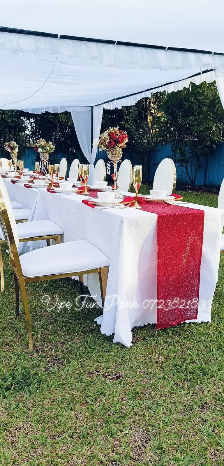 A white marquee tent with a dressed celebration table and gold chairs on the lawn at Vipe Fun Park