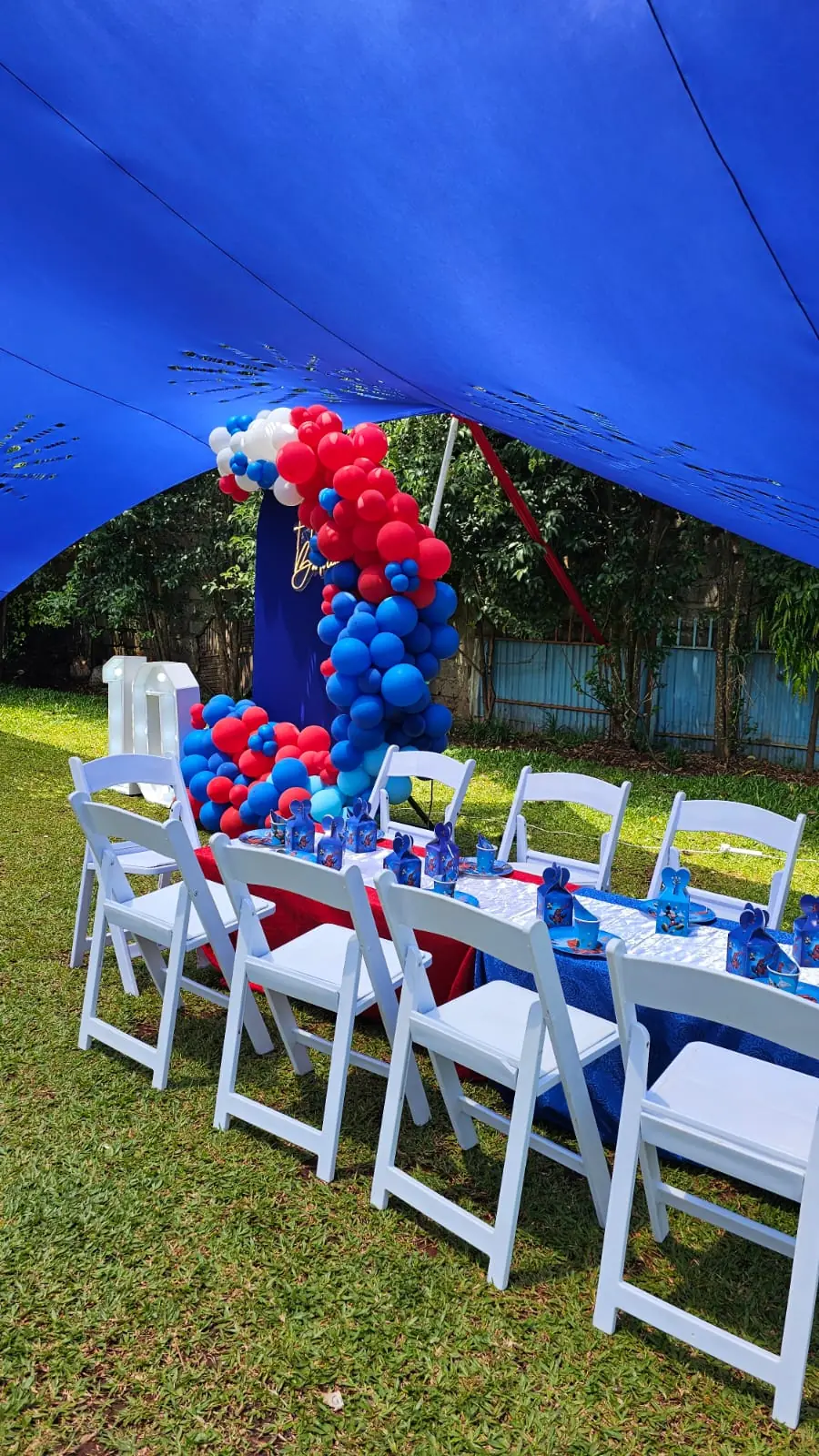 A blue and red birthday table with white chairs and balloon decorations under a blue canopy at Vipe Fun Park
