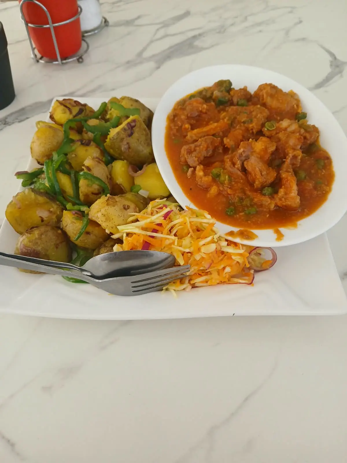 A plate of stewed meat with peas, roast potatoes with green peppers and fresh coleslaw