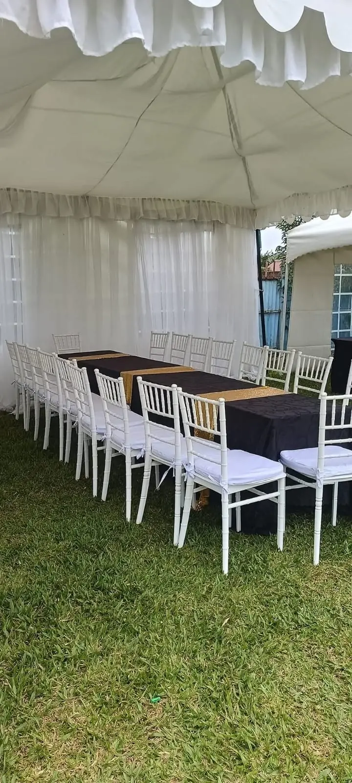 A white dressed event tent with long tables and white chairs on the grass