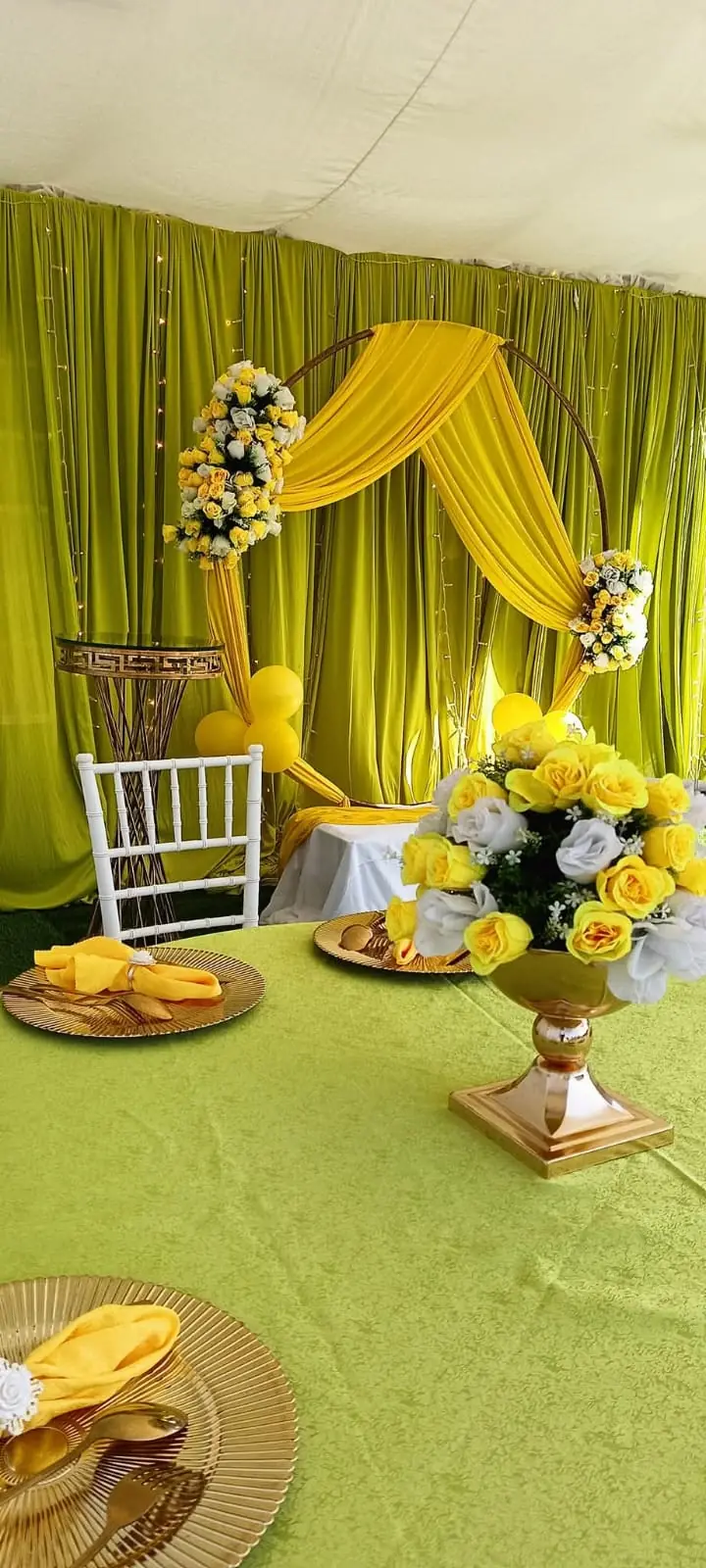 A green and gold celebration table with floral arrangements and a matching decorated backdrop