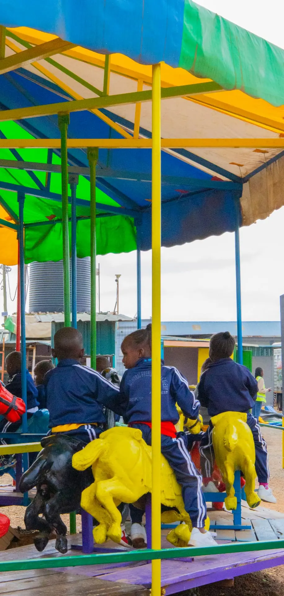 Children seen from behind riding yellow carousel horses beneath a colourful canopy