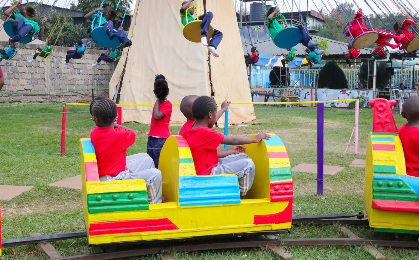 Children seen from behind in colourful train carriages beside the swing ride